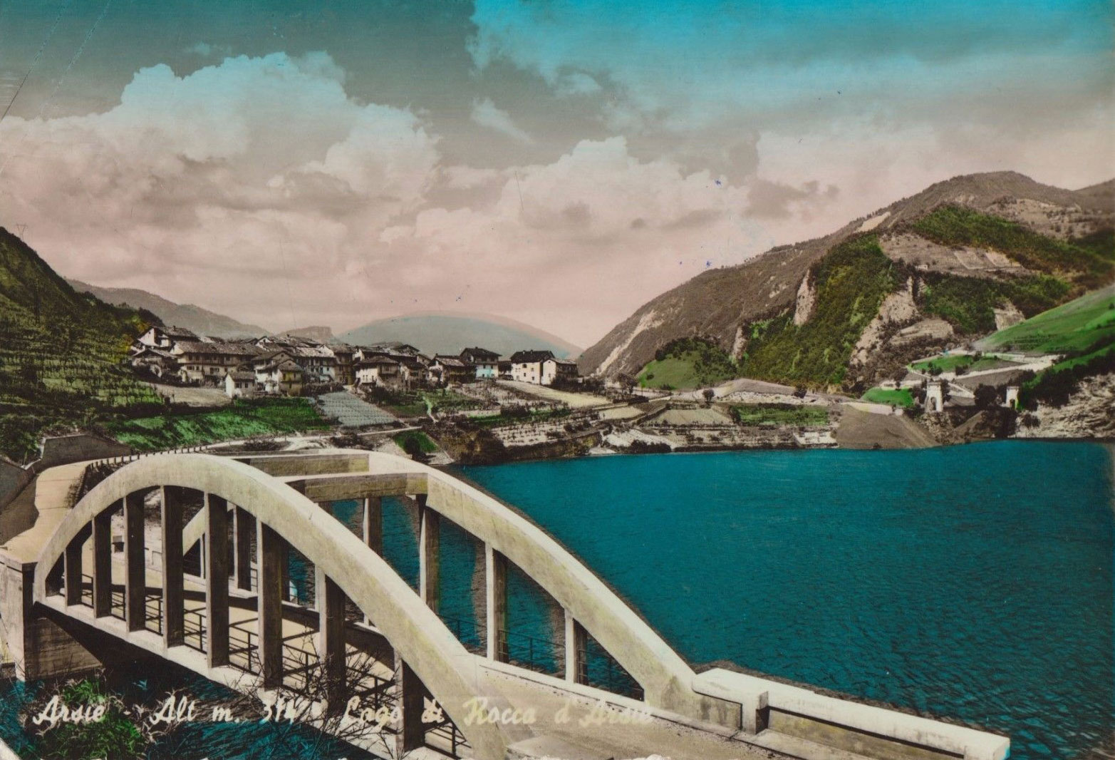 Postcard view of concrete bridge spanning Lake Corlo, with Rocca in background