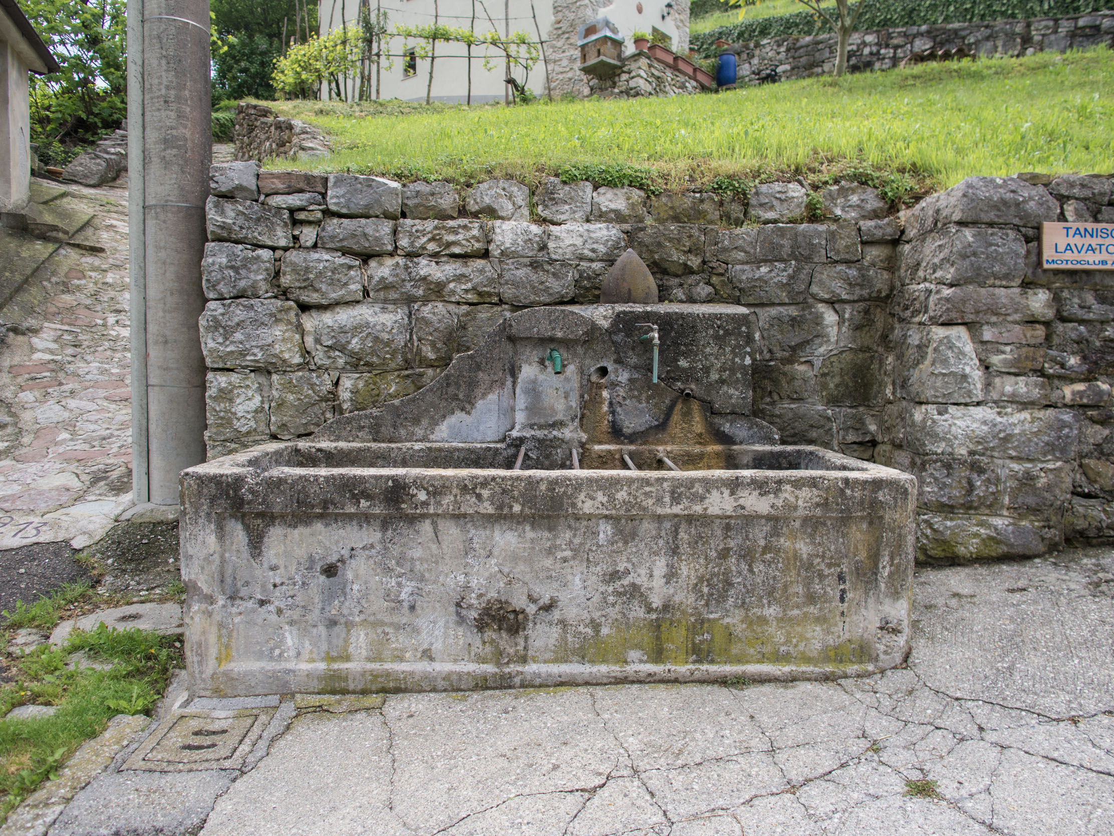 Photo of concrete fountain in front of stone retaining wall, next to Incino's church